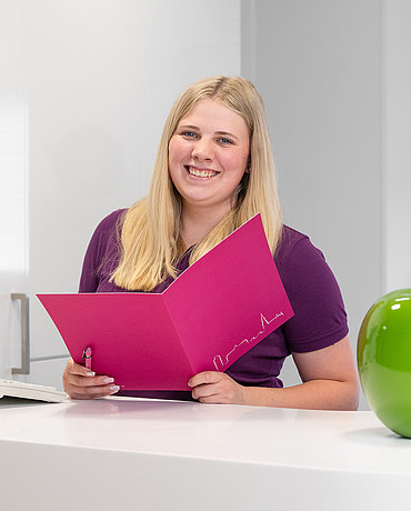 Angestellte Frau Hansen am Empfang der Praxis mit Unterlagen in der Hand