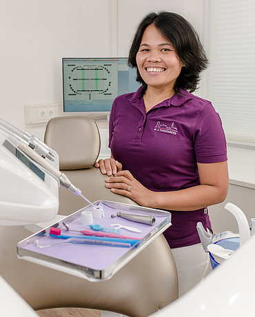 Angestellte Frau Pangilinan-Tackenberg angelehnt an den Behandlungsstuhl im Praxiszimmer